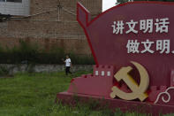 A woman passes near a government propaganda with the words "Speak in civilized manners, act in civilized manners" near the emblem for the Communist Party on the outskirts of Beijing, Thursday, July 25, 2024. (AP Photo/Ng Han Guan)