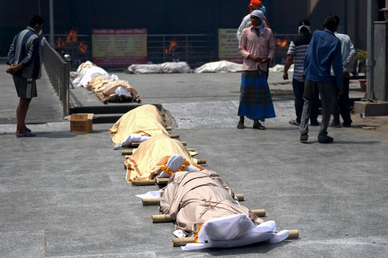 <p>People stand near bodies of Covid-19 coronavirus victims lined up before cremation at a cremation ground in New Delhi on 28 April</p> (AFP via Getty Images)