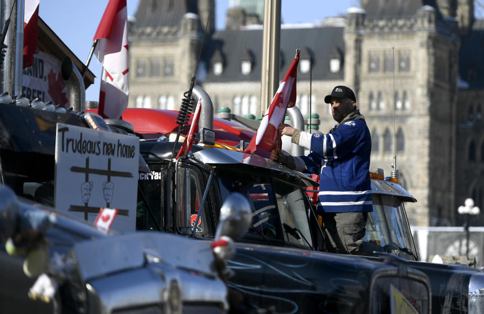 A protester affixes a flag to the top of a truck, parked beside another with a sign calling for the jailing of Prime Minister Justin Trudeau, outside Parliament Hill, as a protest against COVID-19 restrictions continues into its second week in Ottawa on Monday, Feb. 7, 2022. (Justin Tang/The Canadian Press via AP)