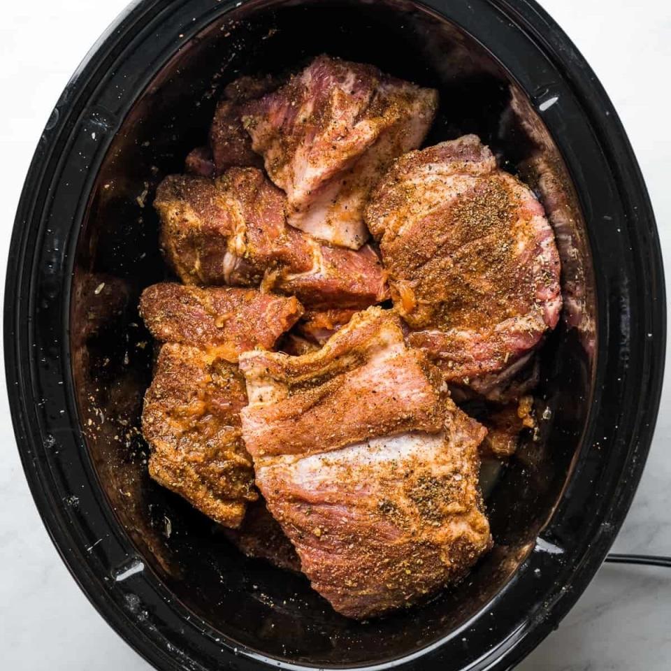 A slow cooker containing seasoned meat ready for cooking
