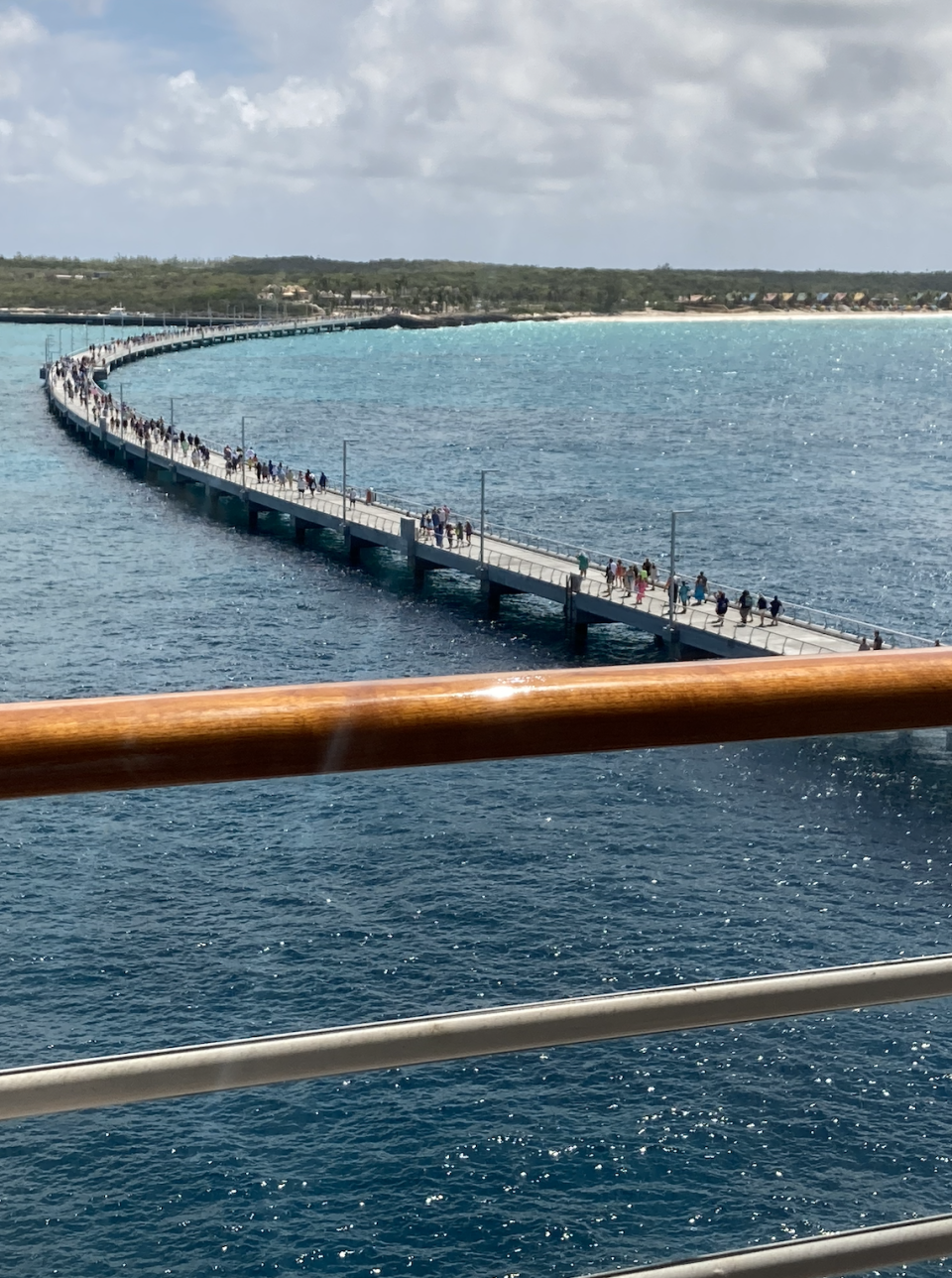 A crowded pier extends into the ocean, connecting to land in the background. Numerous people can be seen walking along the pier