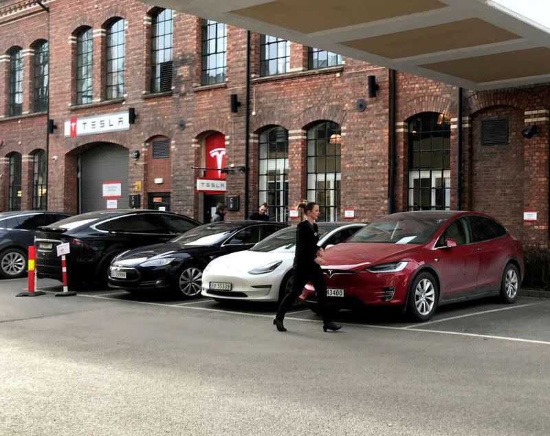 FILE PHOTO: A woman walks past parked Tesla electric vehicles at the delivery site of Tesla in Lillestrom