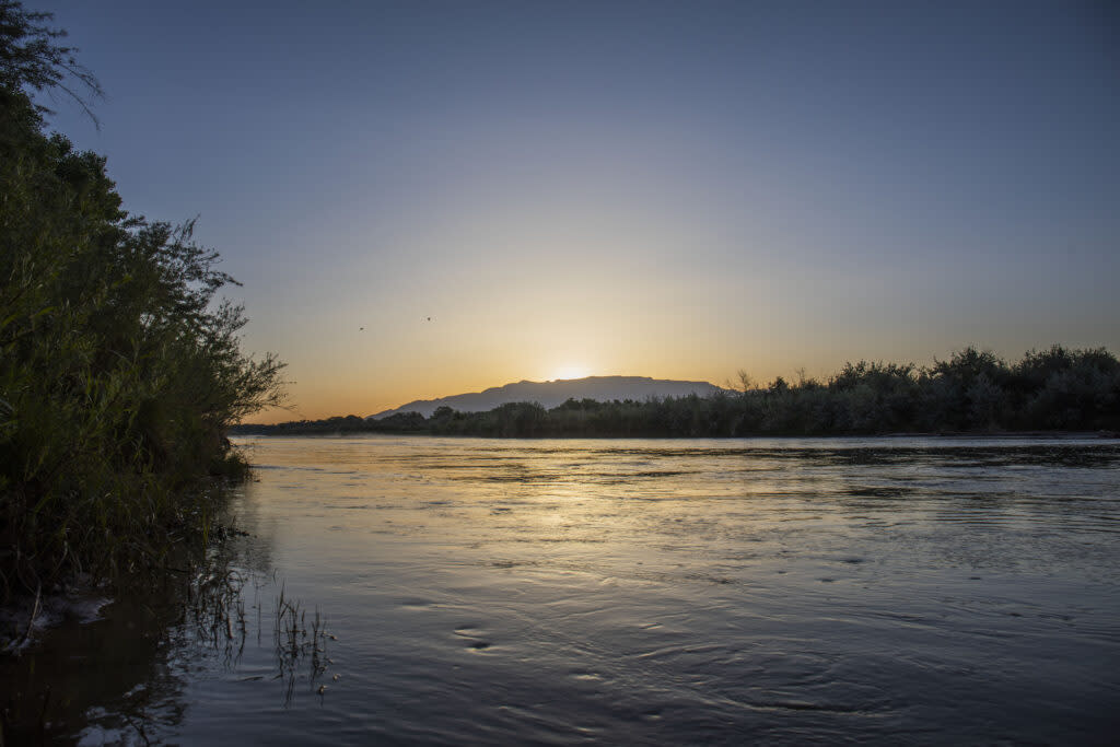 The Rio Grande flows near Albuquerque as the sun rises over the Sandia Mountains.