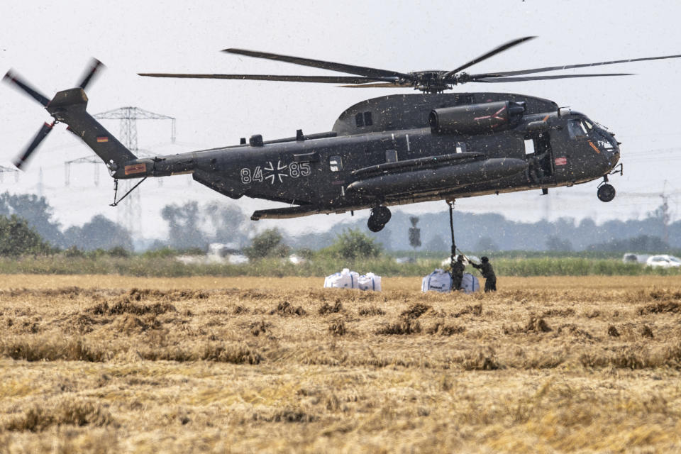 A Bundeswehr CH-53 transport helicopter picks up big bags of ballast in Ergfstadt, Germany, Thursday July 22, 2021, to fly them to the Blessem district to damn up the banks of the Erft river. In the flood disaster area of Erftstadt-Blessem, some residents are being allowed back into their homes to clear debris after heavy rains caused devastating floods. (Marius Becker/dpa via AP)