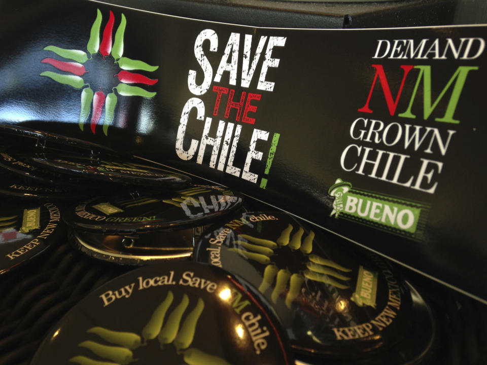 FILE - In this July 31, 2013 file photo, a collection of bumper stickers and buttons promoting New Mexico-grown chile sits on the order counter at Hello Deli restaurant in Albuquerque, N.M. The long-simmering battle between New Mexico and Colorado over which state grows the best chile is heating up. New Mexico Gov. Michelle Lujan Grisham went on the offensive Wednesday, July 10, 2019, after Colorado Gov. Jared Polis proclaimed on Twitter that hot peppers from Pueblo were the best and would be stocked in grocery stores in a four-state region. (AP Photo/Susan Montoya Bryan, File)