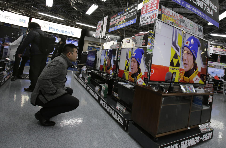 In this Wednesday, Feb. 19, 2014, photo, a shopper at an electronics store in Tokyo watches televisions showing recorded footage from an interview with Japanese ski jumper Noriaki Kasai, who won the silver medal in the large hill and the bronze in team ski jumping at the Sochi Olympics. The program is typical of the localized TV broadcasts in countries throughout the world during the Winter Olympics. (AP Photo/Shizuo Kambayashi)