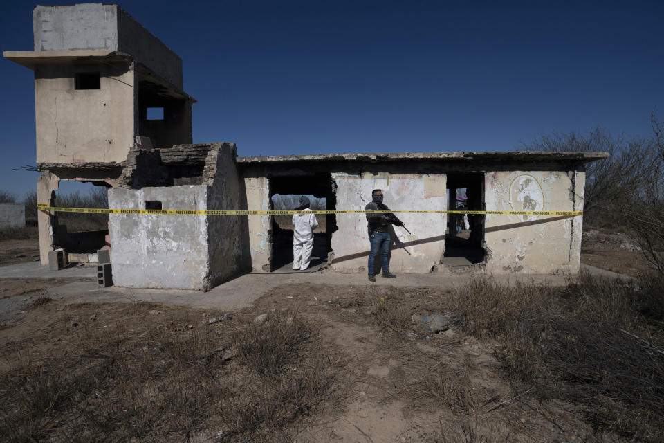 A forensic technician, guarded by a National Guardsman, stands inside a ruined house where bodies were ripped apart and incinerated, on a plot of land referred to as a cartel "extermination site", on the outskirts of Nuevo Laredo, Mexico, Tuesday, Feb. 8, 2022. Until recently, this squat, ruined house was a place where the remains of some of Mexico’s missing were obliterated. (AP Photo/Marco Ugarte)