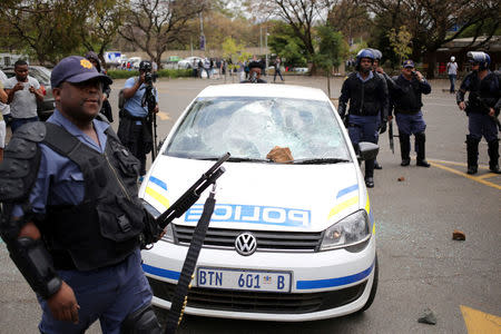 A member of the South African police walks past a police car after it was damaged by students at Johannesburg's University of the Witwatersrand, South Africa. REUTERS/Siphiwe Sibeko