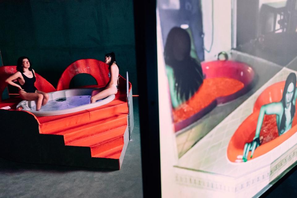 Two women watch a multimedia installation from a hot tub.