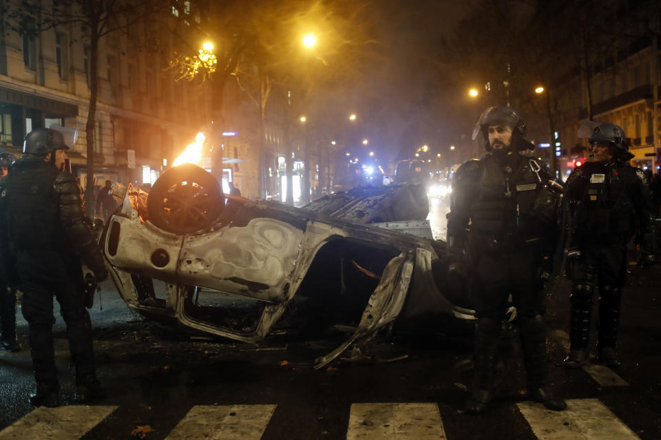 Riot police officers stand next to charred cars near the Trocadero square after a demonstration Saturday, Dec.1, 2018 in Paris. A protest against rising taxes and the high cost of living turned into a riot Saturday in Paris as police fired tear gas and water cannon in street battles with activists wearing the fluorescent yellow vests of a new movement. (AP Photo/Thibault Camus)