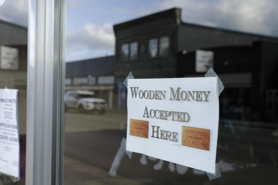 In this May 21, 2020 photo, a sign on a business in Tenino, Wash. says they will be accepting wooden money. In an effort to help residents and local merchants alike get through the economic fallout of the coronavirus pandemic, the small town has issued wooden currency for residents to spend at local businesses, decades after it created a similar program during the Great Depression. (AP Photo/Ted S. Warren)