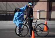 A medical technician performs a nasal swab test on a cyclist queued up in a line with motorists at a COVID-19 testing site near All City Stadium, Thursday, Dec. 30, 2021, in southeast Denver. With the rapid spread of the omicron variant paired with the Christmas holiday, testing sites have been strained to meet demand both in Colorado as well as across the country. (AP Photo/David Zalubowski)