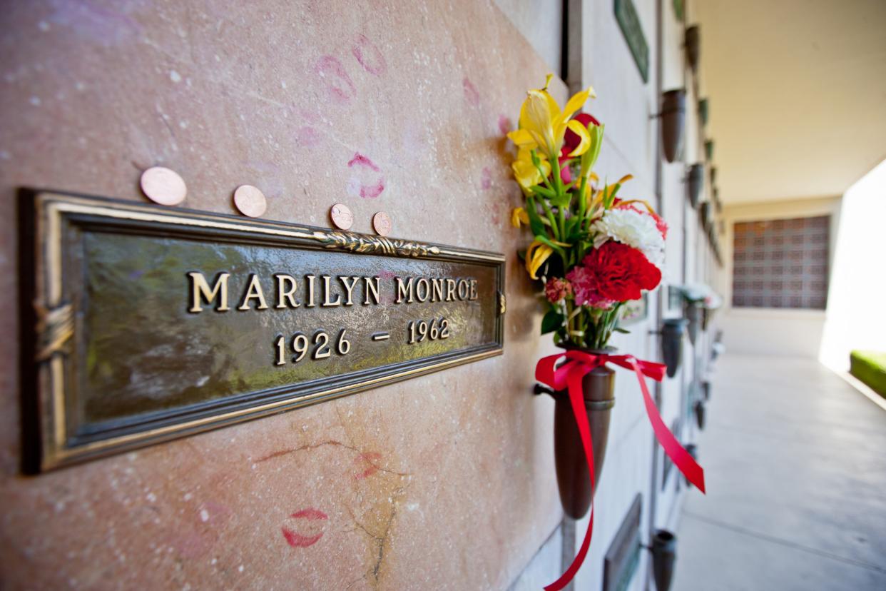 Closeup of Marilyn Monroe's grave at Crypt 24 of Westwood Memorial Park, Los Angeles with pink lipstick kisses on it, four pennies, and flowers in a vase with a blurred background of the other crypts