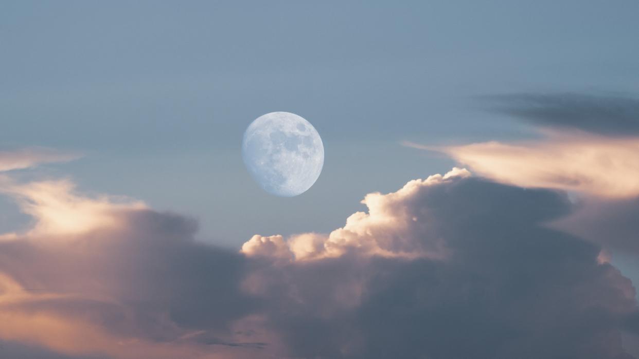  The nearly-full daytime moon hangs dimly in a blue sky near clouds. 