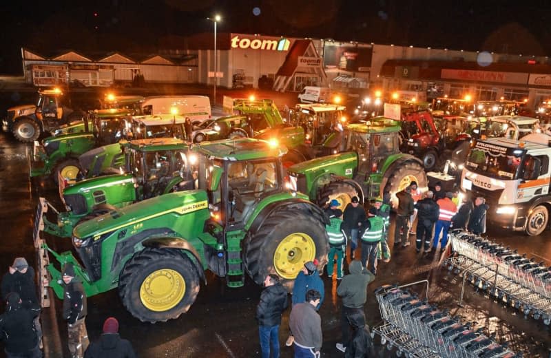 Farmers tractors line up in a parking lot to gather for their journey to Berlin. Thousands of farmers are expected to take part in another major demonstration in Berlin on Monday against the planned end of diesel tax breaks for the agricultural sector. Patrick Pleul/dpa