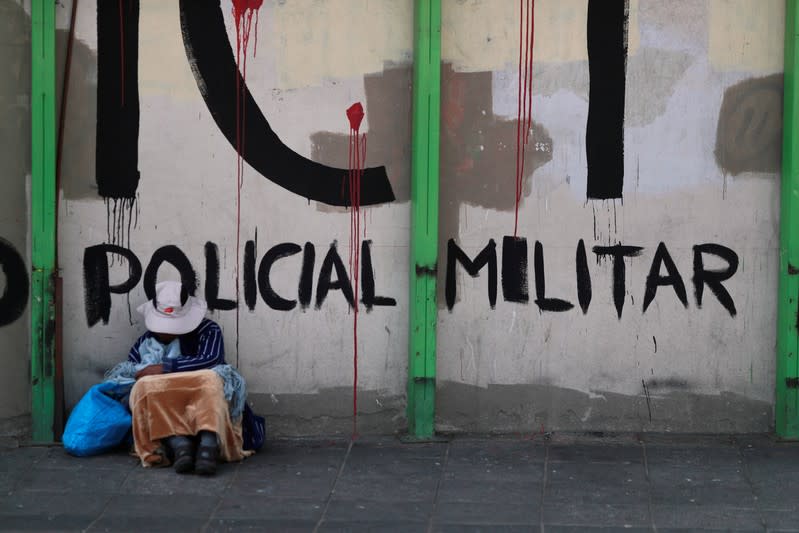 Una mujer sentada junto a una pared con un graffiti que dice "Policia Militar", en La Paz