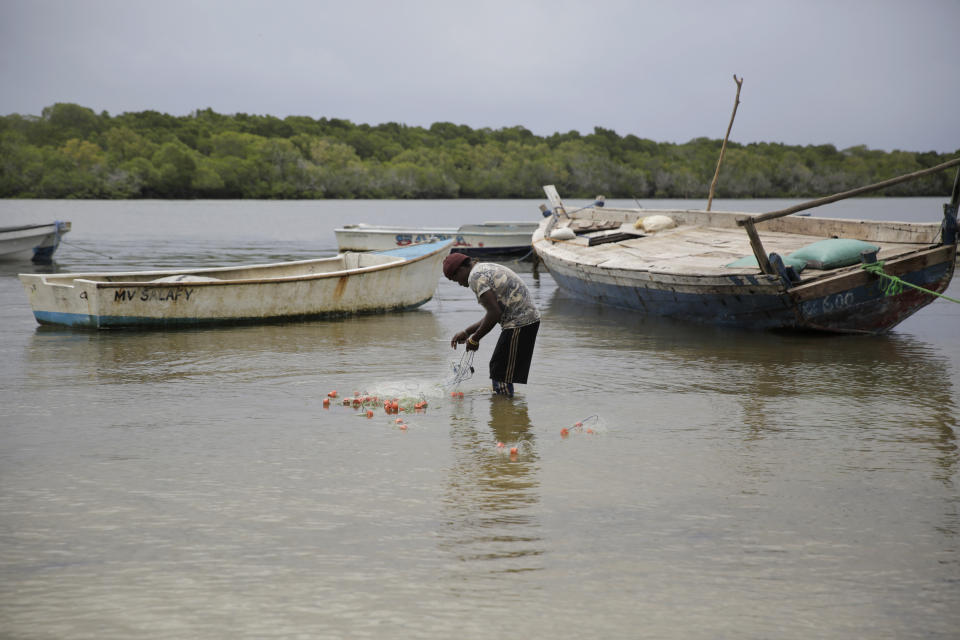 A fisherman repairs his net near mangrove trees in Gazi Bay, Kenya on Sunday, June 12, 2022. (AP Photo/Brian Inganga)