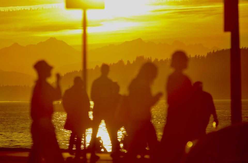 The sun sets behind the Olympic Mountains as people cross a street in Seattle's Alki neighborhood on the last evening of winter on Monday, March 18, 2024. Seattle saw unseasonably warm temperatures as winter turned into spring. The vernal equinox arrives on Tuesday, March 19, marking the start of the spring season for the Northern Hemisphere. (AP Photo/Manuel Valdes)