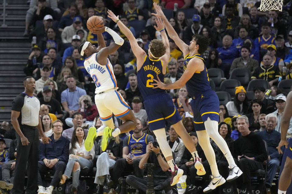 Shai Gilgeous-Alexander, base del Thunder Oklahoma City, encesta frente a Brandin Pdziemski y Dario Saric, de los Warriors de Golden State, en el encuentro del sábado 18 de noviembre de 2023 (AP Foto/Jeff Chiu)