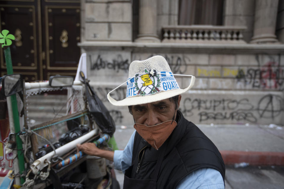 Ice creme vendor Manuel Sosa walks in front of the Congress building area that was damaged during protests in Guatemala City, Sunday, Nov. 22, 2020. Protesters broke into the building and set it partially on fire amid growing demonstrations against President Alejandro Giammattei and the legislature for approving a controversial budget that cut educational and health spending. (AP Photo/Moises Castillo)