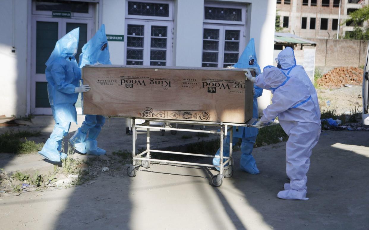 Ambulance drivers in protective gear carry the coffin of a woman who died from coronavirus - Farooq Khan/Shutterstock