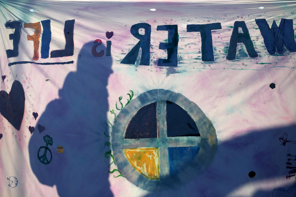 A camper is silhouetted behind a flag reading "Water Is Life" in the Oceti Sakowin camp.