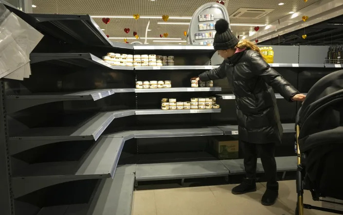 A woman shops at a grocery store with nearly empty shelves. 