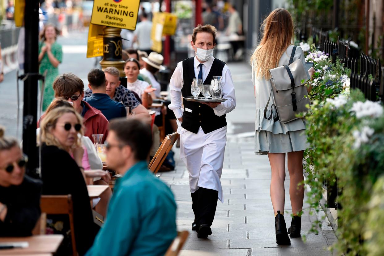 A waiter wears a face mask while serving customers at a restuarant in Soho, London, 20 September 2020 (AFP via Getty Images)