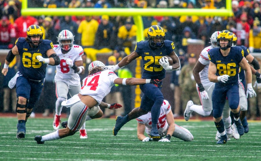 FILE – Michigan running back Hassan Haskins (25) breaks a tackle from Ohio State safety Ronnie Hickman (14) in the fourth quarter of an NCAA college football game in Ann Arbor, Mich., Saturday, Nov. 27, 2021. Michigan won 42-27. (AP Photo/Tony Ding, File)