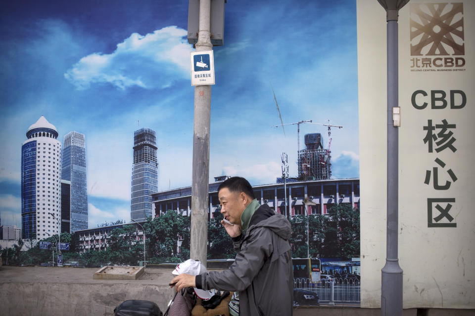 A man uses his mobile phone in front of a billboard at a construction site in Beijing, Thursday, May 16, 2019. Figures released on Wednesday showed China's factory output and consumer spending weakened in April as a tariff war with Washington intensified, adding to pressure on Beijing to shore up shaky economic growth. (AP Photo/Mark Schiefelbein)