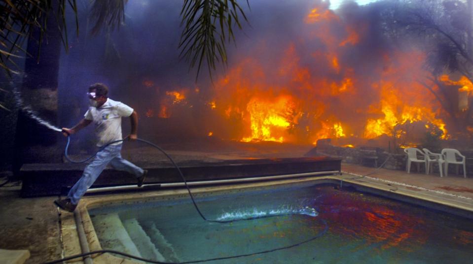 A man with a hose runs from flames outside his house