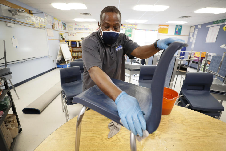 Des Moines Public Schools custodian Tracy Harris cleans a chair in a classroom at Brubaker Elementary School, Wednesday, July 8, 2020, in Des Moines, Iowa. School districts that plan to reopen classrooms in the fall are wrestling with whether to require teachers and students to wear face masks. In Iowa, among other places, where Democratic-leaning cities like Des Moines and Iowa City have required masks to curb the spread of the coronavirus, while smaller, more conservative communities have left the decision to parents. (AP Photo/Charlie Neibergall)