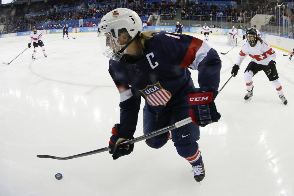 Meghan Duggan of the Untied States talks control of the puck as Evelina Raselli of Switzerland chases her during the third period of the 2014 Winter Olympics women's ice hockey game at Shayba Arena, Monday, Feb. 10, 2014, in Sochi, Russia. (AP Photo/Matt Slocum)