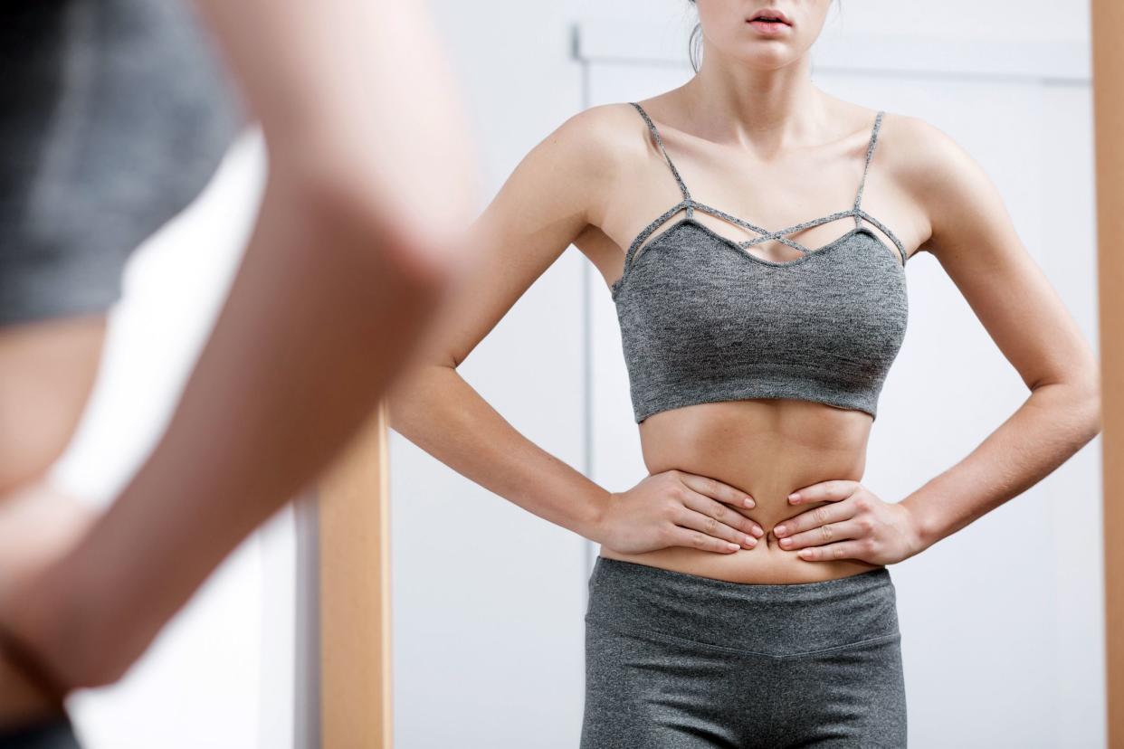 woman looking in mirror and squeezing waist very tightly