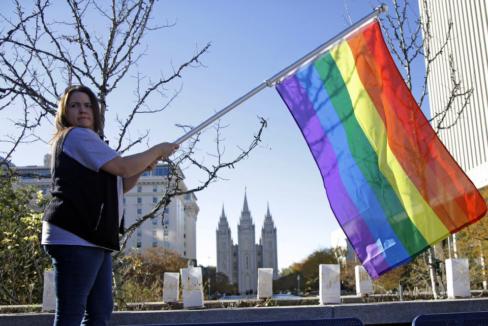 FILE - In this Nov. 14, 2015 file photo, Sandy Newcomb poses for a photograph with a rainbow flag as people gather for a mass resignation from The Church of Jesus Christ of Latter-day Saints in Salt Lake City. The Church of Jesus Christ of Latter-day Saints is repealing rules unveiled in 2015 that banned baptisms for children of gay parents and made gay marriage a sin worthy of expulsion. The surprise announcement Thursday, April 4, 2019, by the faith widely known as the Mormon church reverses rules that triggered widespread condemations from LGBTQ members and their allies. (AP Photo/Rick Bowmer, File)