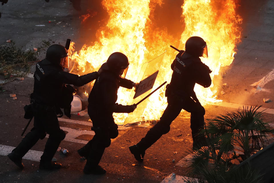 Police officers run past a burning barricade on the fifth day of protests over the conviction of a dozen Catalan independence leaders in Barcelona, Spain, Friday, Oct. 18, 2019. Tens of thousands of flag-waving demonstrators demanding Catalonia's independence and the release from prison of their separatist leaders have flooded downtown Barcelona. The protesters have poured into the city after some of them walked for three days in "Freedom marches" from towns across the northeastern Spanish region, joining students and workers who have also taken to the streets on a general strike day. (AP Photo/Manu Fernandez)
