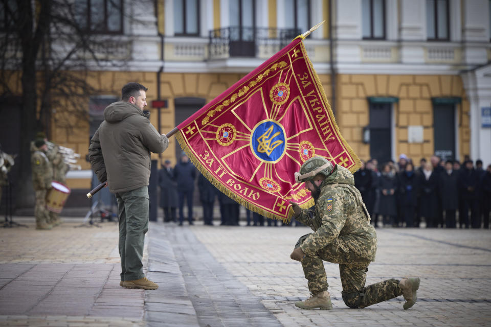 Ukrainian President Volodymyr Zelenskyy, left, holds the flag of a military unit as an officer kisses it, during commemorative event on the occasion of the Russia Ukraine war one year anniversary in Kyiv, Ukraine, Friday, Feb. 24, 2023. (Ukrainian Presidential Press Office via AP)