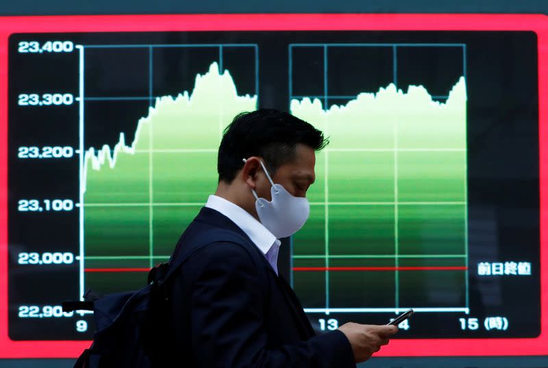 FILE PHOTO: A man wearing a protective face mask walks past a screen displaying a graph showing recent Nikkei share average outside a brokerage, amid the coronavirus disease (COVID-19) outbreak, in Tokyo