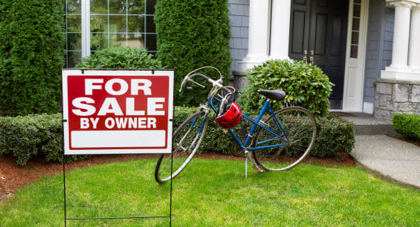 Closeup view of Modern Suburban Home with for Sale Real Estate Sign in front yard and bicycle and house in background