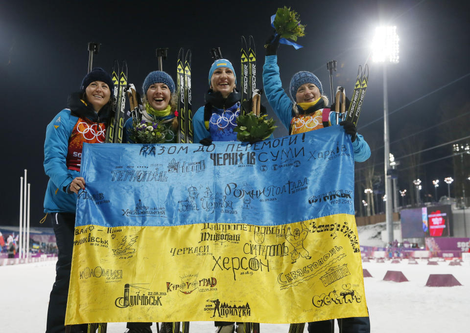 Ukraine's relay team Vita Semerenko, Juliya Dzhyma, Olena Pidhrushna and Valj Semerenko, from left, celebrate with a Ukrainian flag with writings on it after winning the gold during the women's biathlon 4x6k relay, at the 2014 Winter Olympics, Friday, Feb. 21, 2014, in Krasnaya Polyana, Russia. (AP Photo/Dmitry Lovetsky)