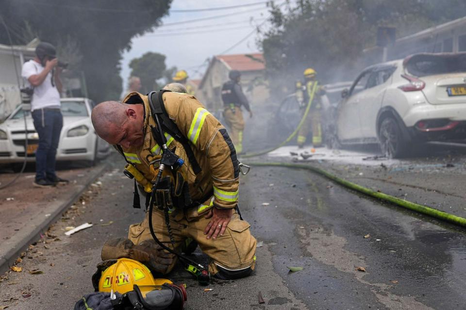 PHOTO: An Israeli firefighter kneels to compose himself after he and his colleagues extinguished cars burning after being struck by rockets fired from the Gaza Strip in Ashkelon, Israel, Oct. 9, 2023. (Ohad Zwigenberg/AP)