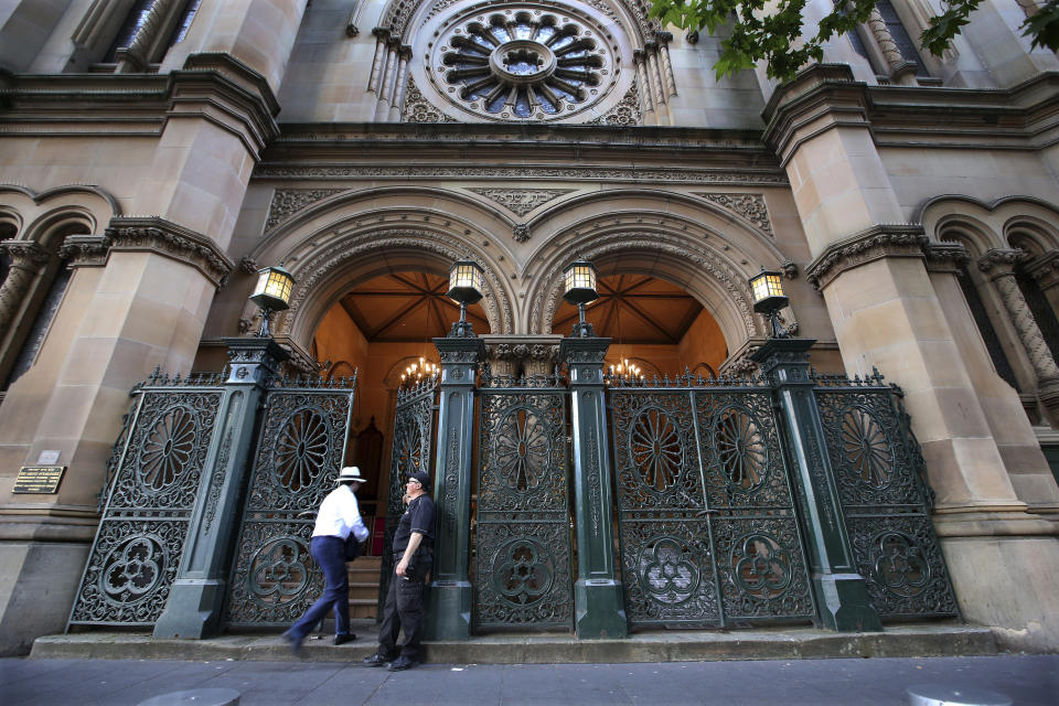 In this Friday, Nov. 2, 2018, photo a security man, right, opens a heavy gate to let a man in for the evening service at The Great Synagogue in Sydney. Synagogues, mosques, churches and other houses of worship are routinely at risk of attack in many parts of the world. And so worshippers themselves often feel the need for visible, tangible protection even as they seek the divine. (AP Photo/Rick Rycroft)