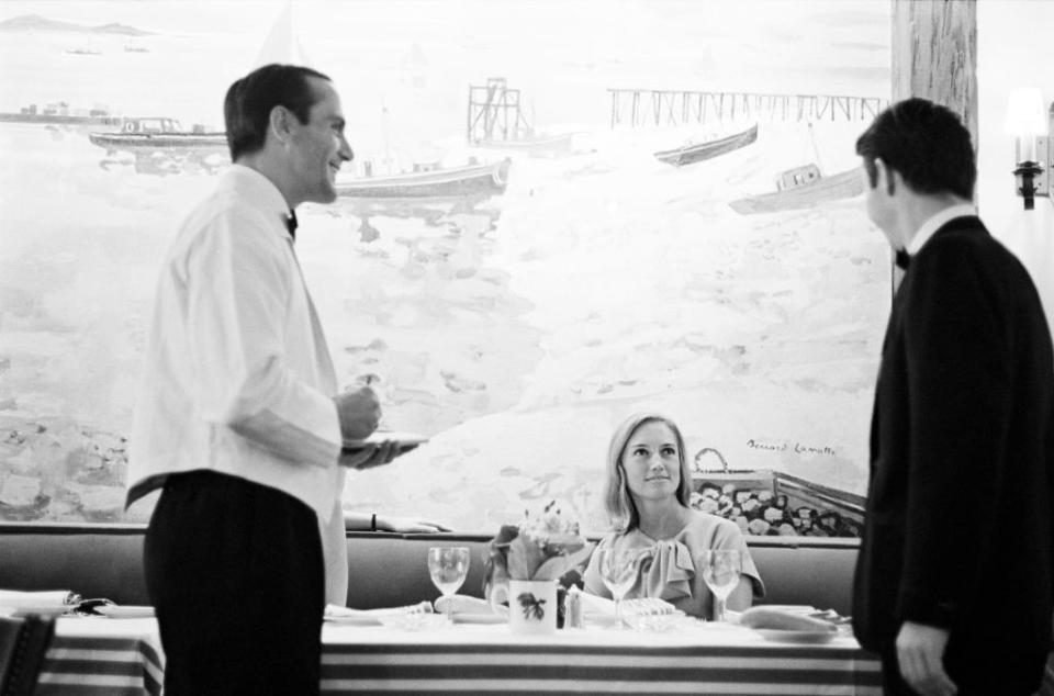 As a waiter stands by, American advertising executive Mary Wells sits at a table ans speaks with an unidentified man at the restaurant La Cote Basque (at 60 West 55th Street), New York, New York, September 1966. (Photo by Susan Wood/Getty Images)