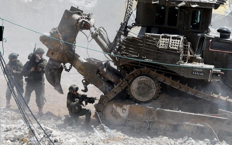 Israeli soldiers take cover behind a military bulldozer during an Israeli raid in Deir al-Ghusun, in the Israeli occupied West Bank, May 4, 2024.