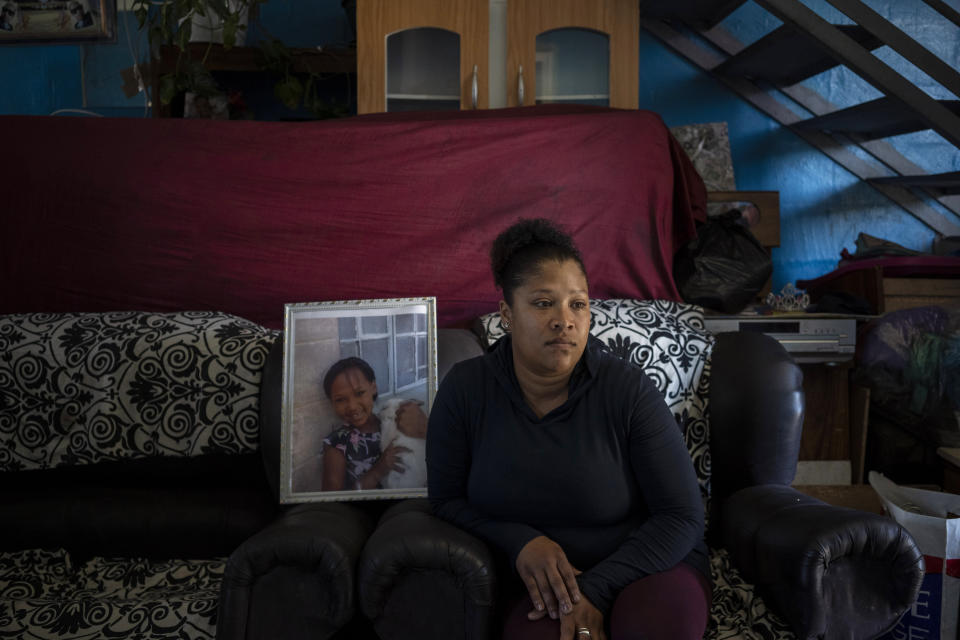 Carmen van Wyk sits on a sofa in her house next to a framed photograph of her daughter, Tazne, in Cape Town, South Africa, on Sept. 10, 2020. The 8-year-old girl was abducted next to her house and her body was found two weeks later next to a highway. She had been raped and murdered. (AP Photo/Bram Janssen)