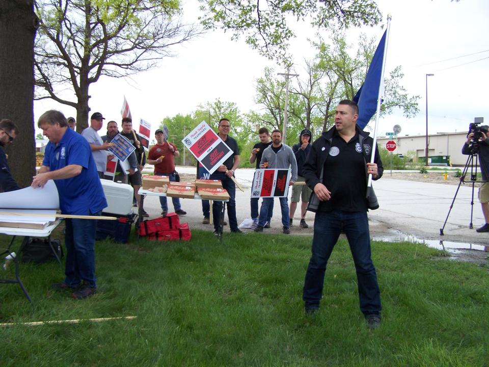 Teamsters Local 90 Principal Officer Alano De La Rosa carries the union flag for a practice picket Wednesday at Plumb Supply in Des Moines. The union and company officials are negotiating a new contract with hopes that a strike can be averted.