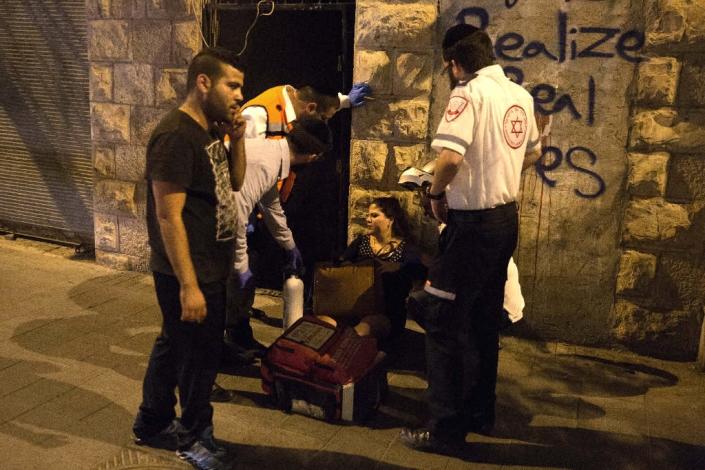 A woman is treated by medics at the site where a knife-wielding man stabbed and wounded a woman near Jerusalem's central bus station on October 14, 2015 (AFP Photo/Menahem Kahana)