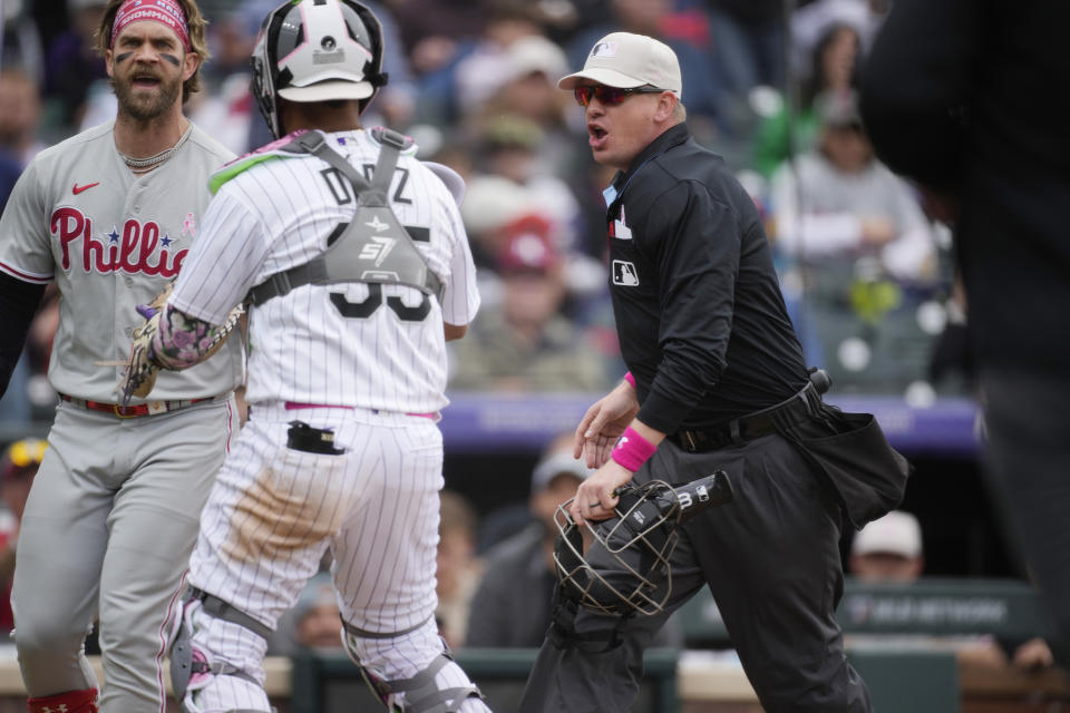 Philadelphia Phillies' Bryce Harper, left, is stopped by Colorado Rockies catcher Elias Diaz, second from left, as home plate umpire Ryan Wills, right, looks on as Harper reacts after Rockies elief pitcher Jake Bird after Bird gestured toward the Phillies' dugout after retiring Phillies' Bryson Stott to end the top of the seventh inning of a baseball game Sunday, May 14, 2023, in Denver. (AP Photo/David Zalubowski)