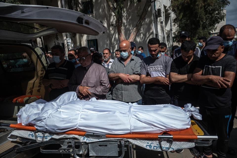 People pray over a body wrapped in white on a gurney