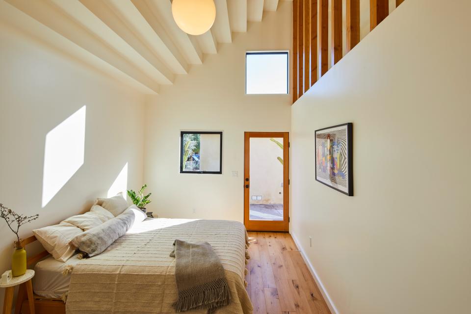 The stepped ceiling of one of the two bedrooms in the ADU contrasts with the verticality of the tall walls and exposed wood studs at the upper level of the wall.